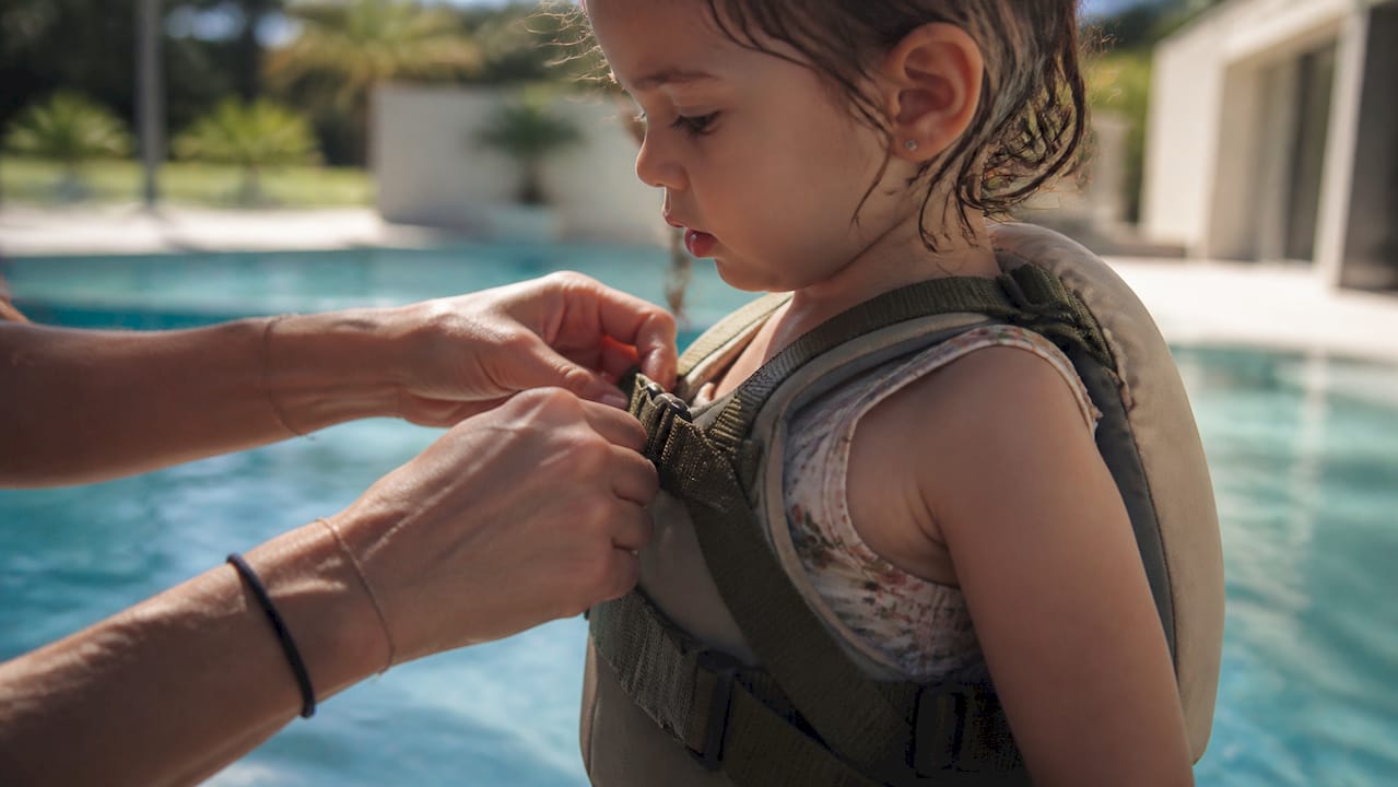 Elternteil stellt die Gurte der Schwimmhilfe des Kindes ein