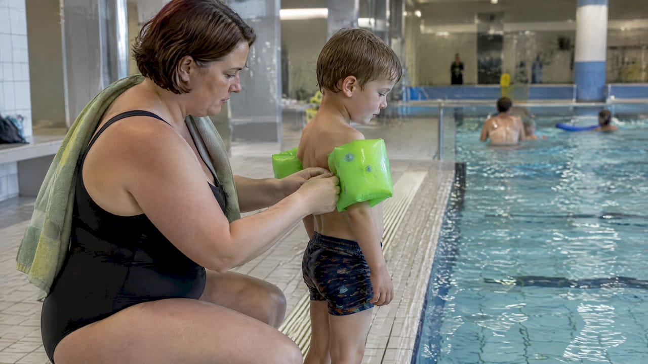 Eine Mutter zieht ihrem Kind am Beckenrand die Schwimmflügel an
